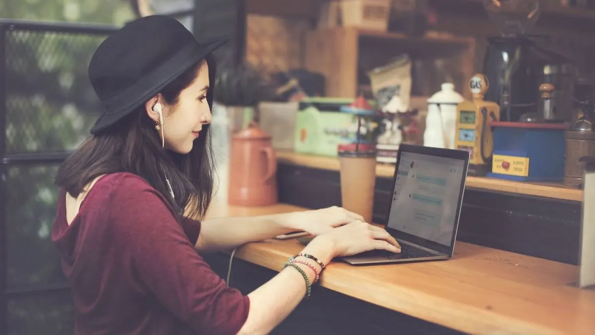 Frau mit schwarzem Hut arbeitet konzentriert am Laptop in gemütlichem Café.