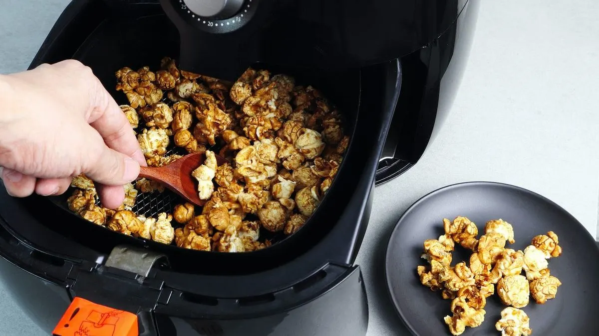 Karamellpopcorn wird mit einem Holzlöffel aus einer Heißluftfritteuse  genommen und auf einem grauen Teller serviert.