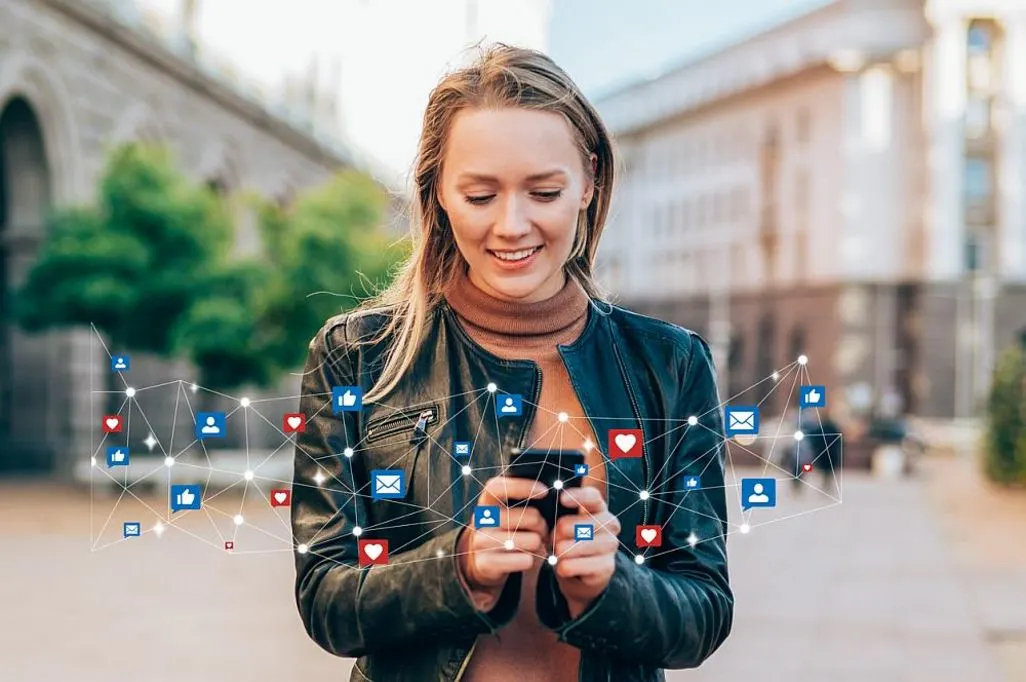 Eine Frau haelt ein Smartphone in der Hand, umgeben von Symbolen fuer Social Media