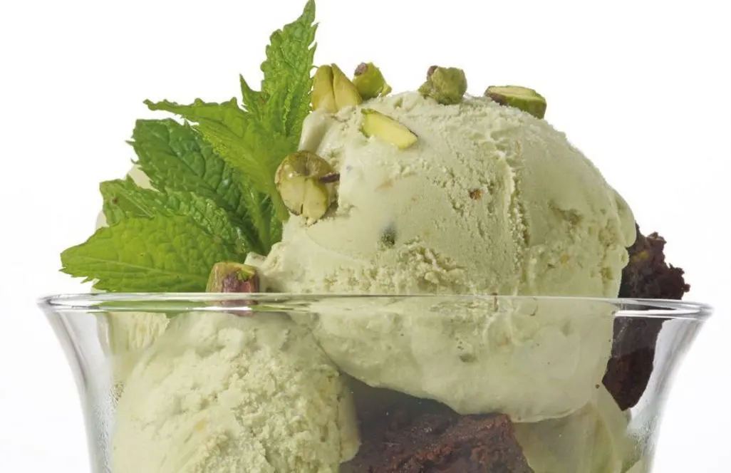 Pistazieneis mit Schokokuchenstueck und Minze in einer Glasschuessel serviert