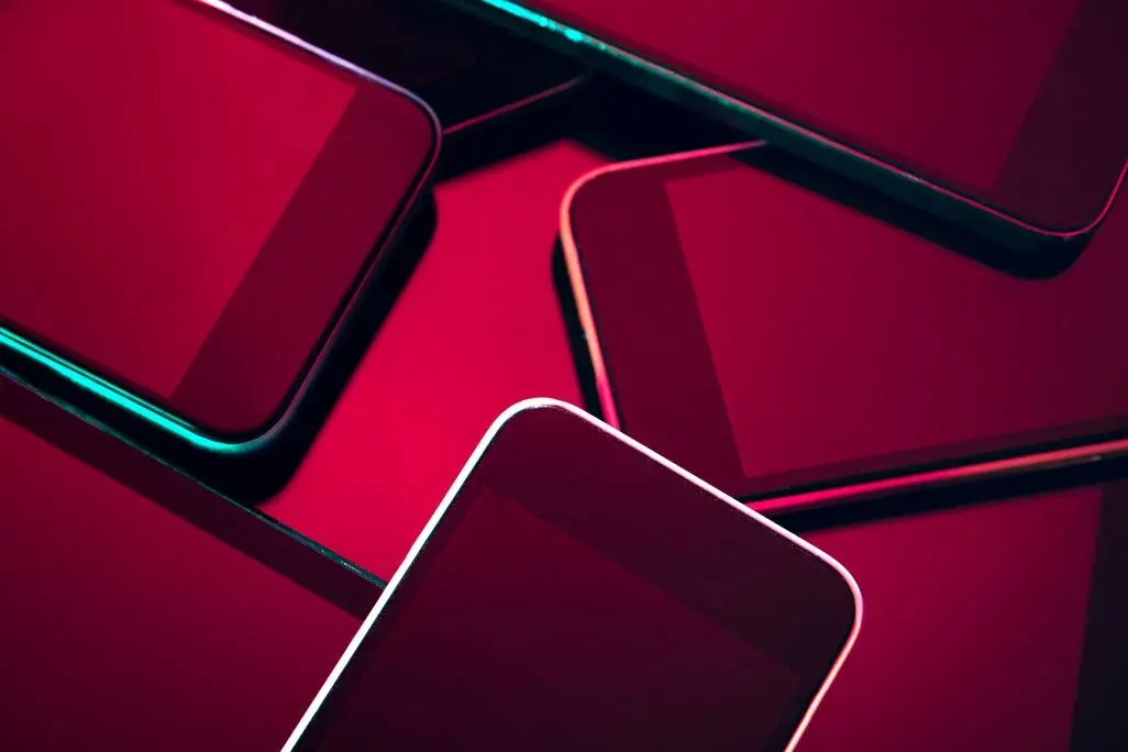 Mehrere Smartphones mit schwarzen Bildschirmen, dramatisch in Rot- und Neontönen beleuchtet, überlappend angeordnet.