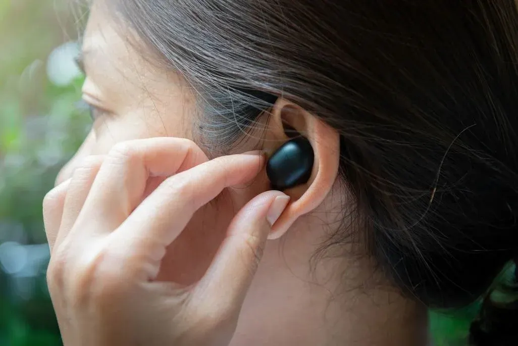 Person setzt schwarzen In‑Ear‑Kopfhörer ins linke Ohr.