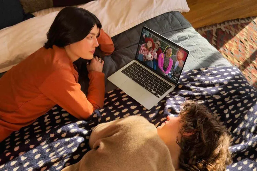 Zwei Mädchen liegen auf einem Bett, zwischen ihnen ein neues MacBook Air mit M5-Chip.