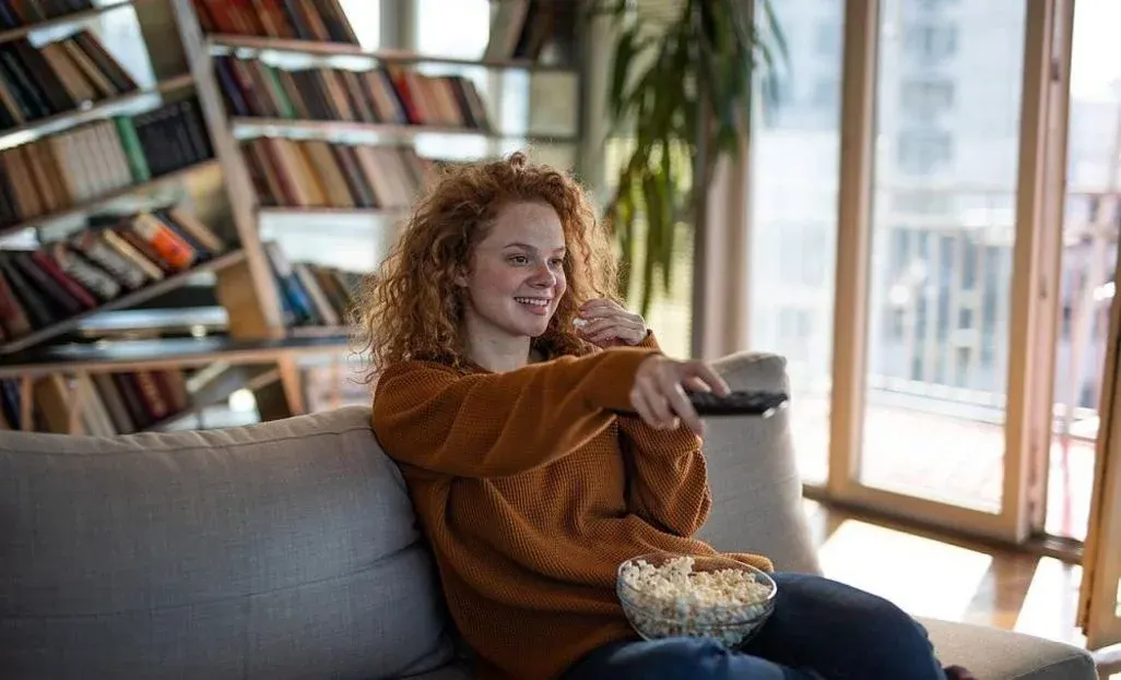 Laechelnde Frau isst Popcorn und nutzt eine Fernbedienung