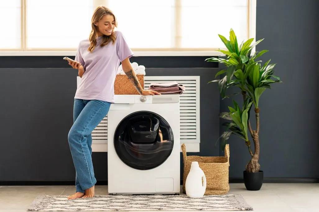Frau lehnt mit Handy an Waschmaschine im modernen Haushalt.
