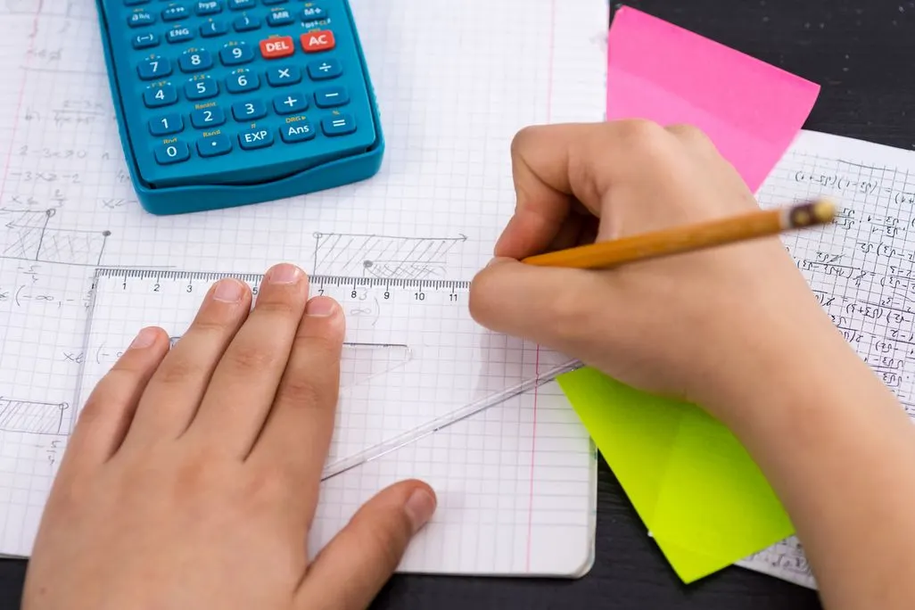 Haende arbeiten mit Taschenrechner, Lineal und Bleistift an mathematischen Berechnungen.