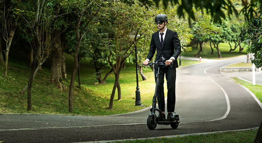 Ein Elektroroller auf einem Weg, umgeben von Bäumen und Grünflächen. Der Weg schlängelt sich durch den Park.