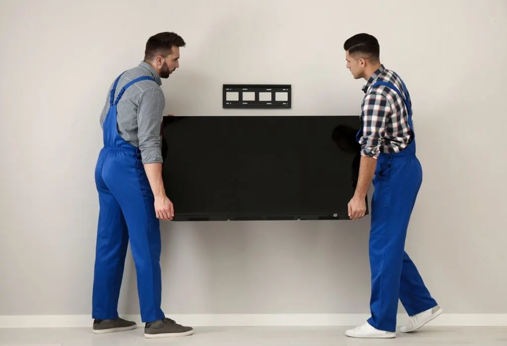 Zwei Personen heben einen Fernseher vor eine Wandhalterung.