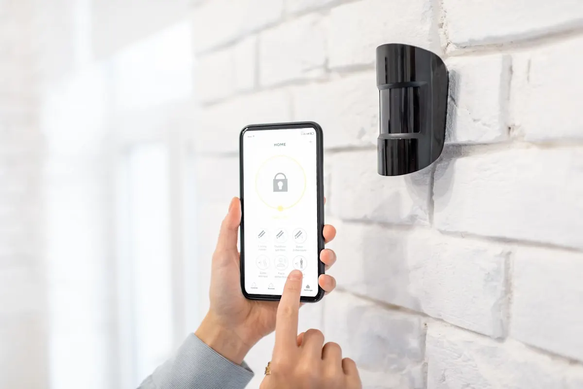 Hand hält Smartphone mit App vor einen Bewegungsmelder an der Wand.
