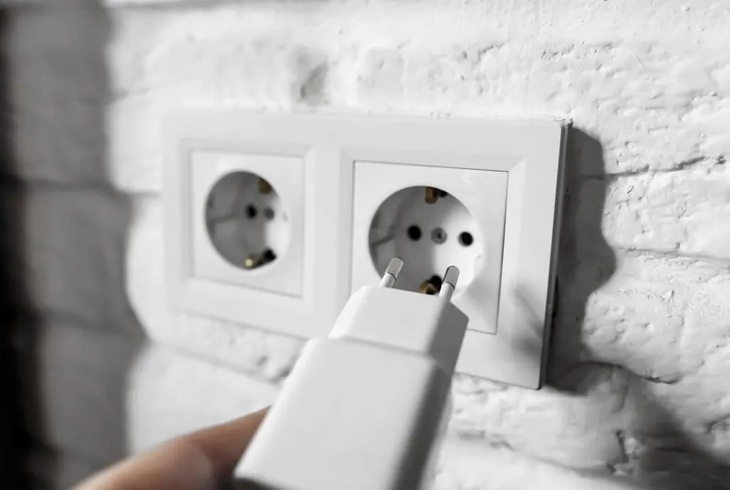 Hand steckt einen Netzstecker in eine Steckdose an einer weissen Wand
