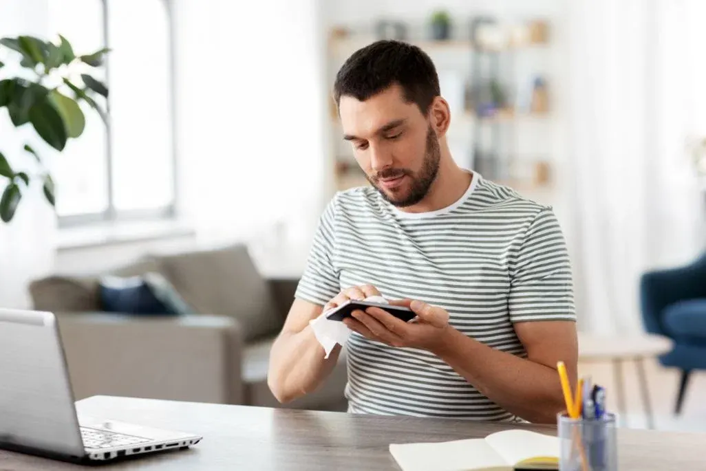 Mann reinigt sein Smartphone mit einem Mikrofasertuch.