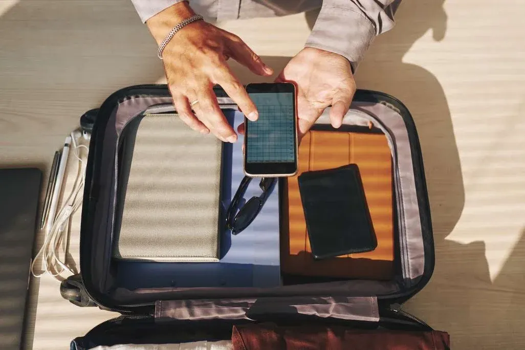 Mann tippt am Smartphone über einem gepackten Koffer.