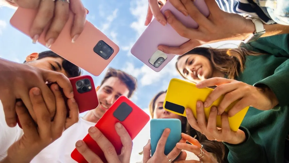 Mehrere Menschen halten bunte Smartphones in die Mitte und bilden einen Kreis.