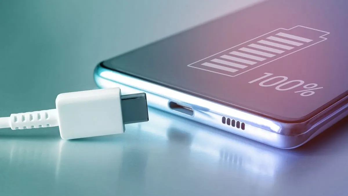 Nahaufnahme eines Smartphones mit Ladesymbol auf dem Display und Ladekabel kurz vor dem Anschluss.
