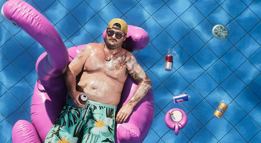 Cal liegt auf einem aufblasbaren Flamingo in einem Pool, umgeben von an der Oberfläche schwimmenden Dosen.