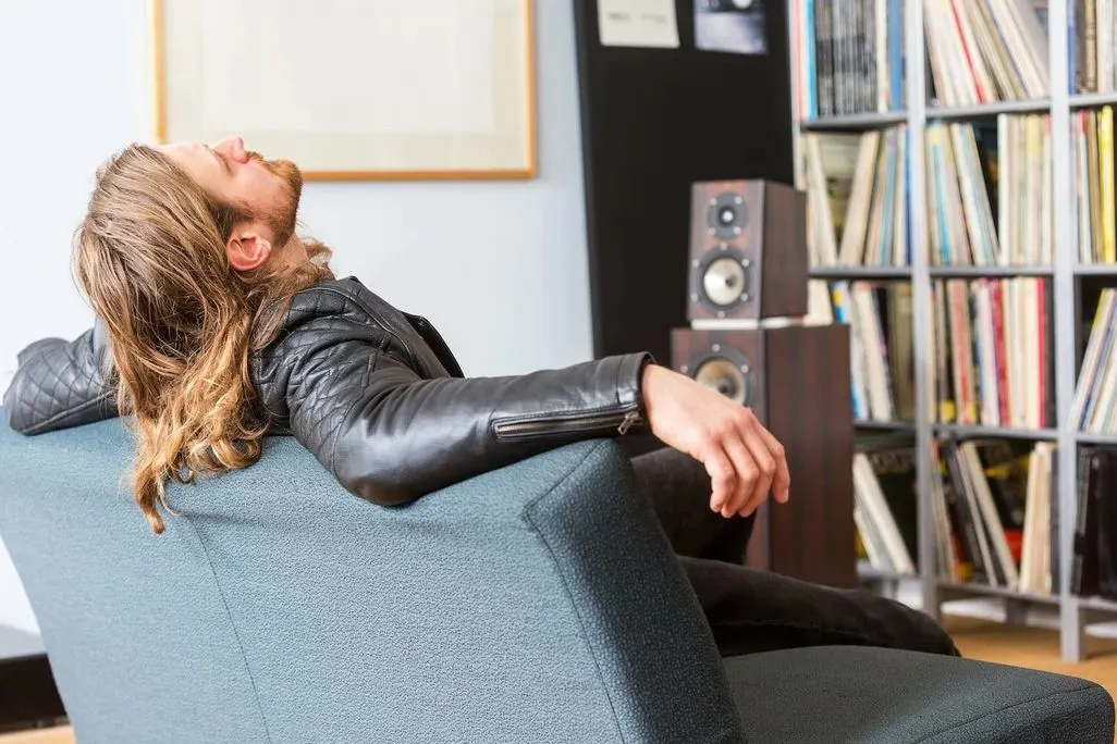 Eine Person lehnt entspannt auf einem Sofa vor einem Regal mit Schallplatten und Lautsprechern