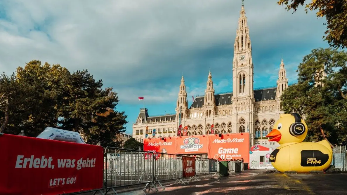 Vor dem Wiener Rathaus ist der Eingang zur Game City: davor stehen Absperrgitter, rote Werbebanner von MediaMarkt und eine große gelbe FM4 Quietschente mit Kophörern..