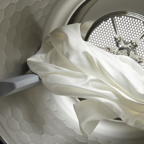 Ein Blick in eine Waschmaschine zeigt ein weißes Tuch vor einer perforierten Trommel und einer grauen, wabenförmigen Innenwand.