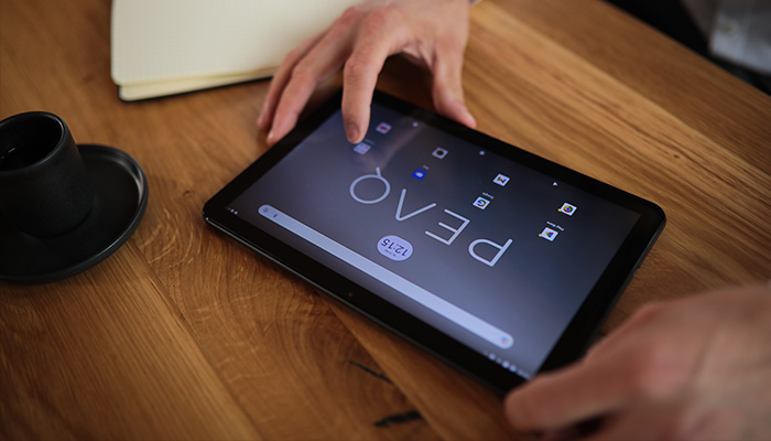 Zwei Hände bedienen ein PEAQ Android-Tablet auf einem Holztisch,  neben einer schwarzen Kaffeetasse.