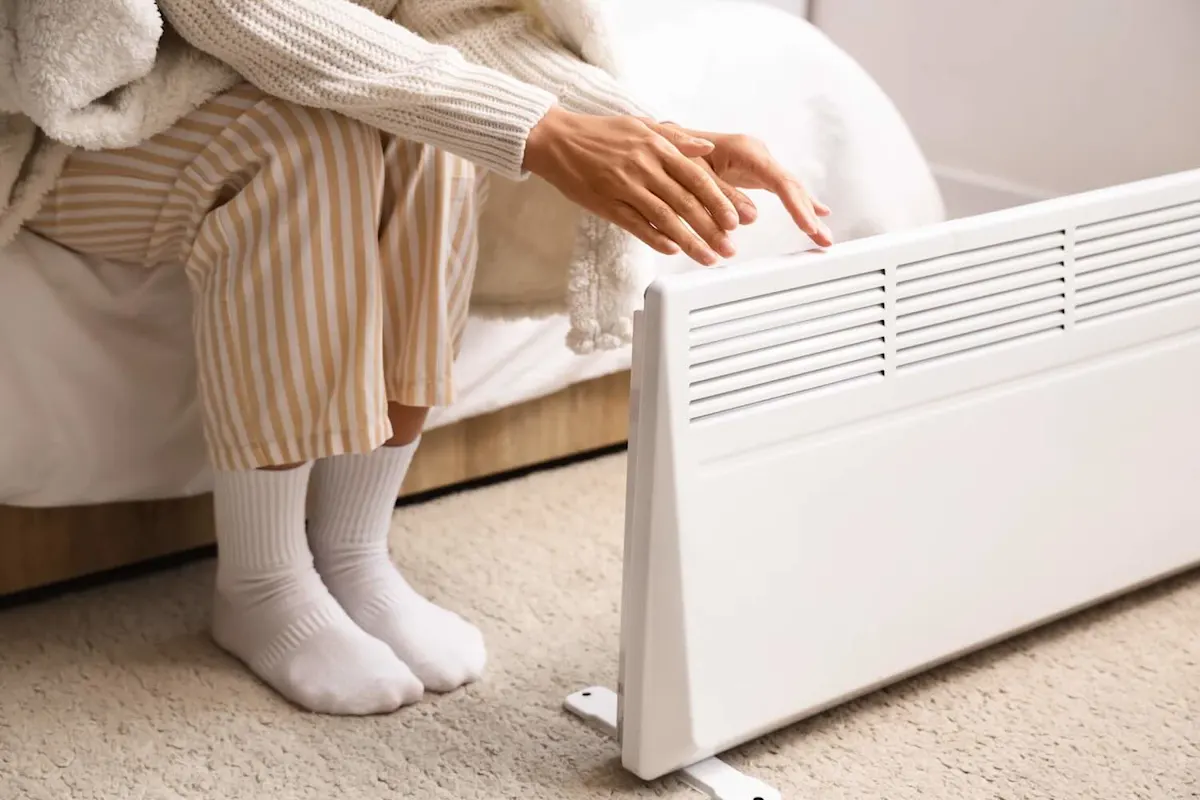 Eine warm bekleidete Person wärmt ihre Hände an einem Konvektor.