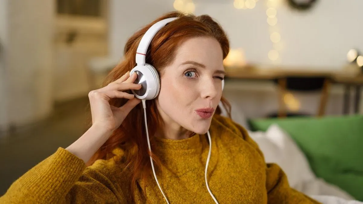 Eine Person mit langen roten Haaren trägt weiße Kopfhörer und berührt sie mit einer Hand.