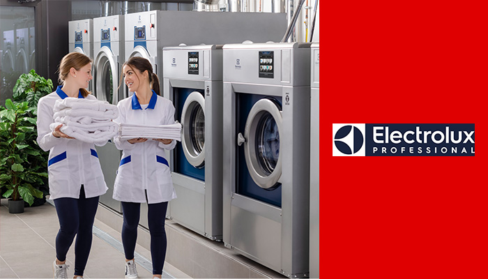 2 Frauen in einer Wäscherei mit Handtüchern in der Hand, Waschmaschinen und Trockner im Hintergrund. Rechts befindet sich das Electrolux Logo