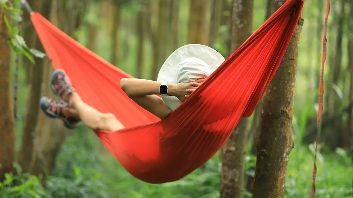 Person mit Hut entspannt in einer roten Hängematte im Wald und trägt eine Smartwatch.