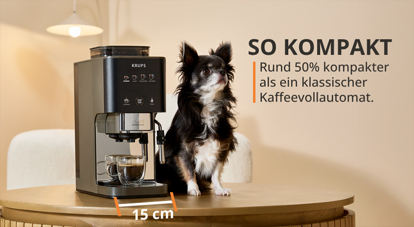 Krups Kaffeemaschine neben Hund auf Holztisch. SO KOMPAKT: Rund 50% kompakter als klassischer Kaffeevollautomat. 15 cm Breite.