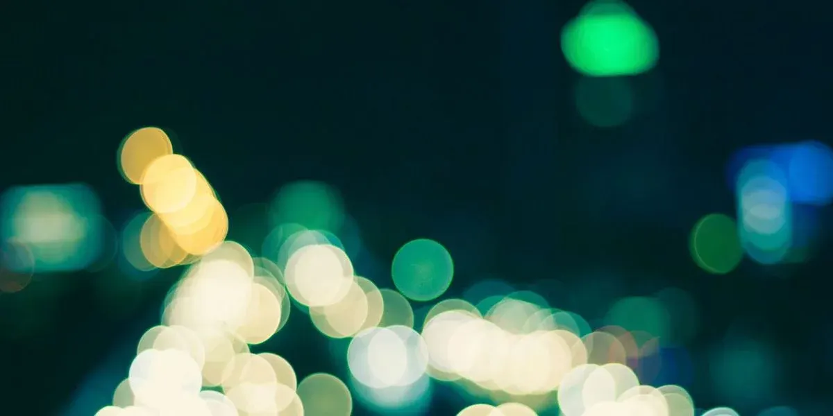 Verschwommene gelbe, weiße, grüne und blaue Lichter erzeugen einen Bokeh-Effekt vor dunklem Hintergrund, unten dichter.