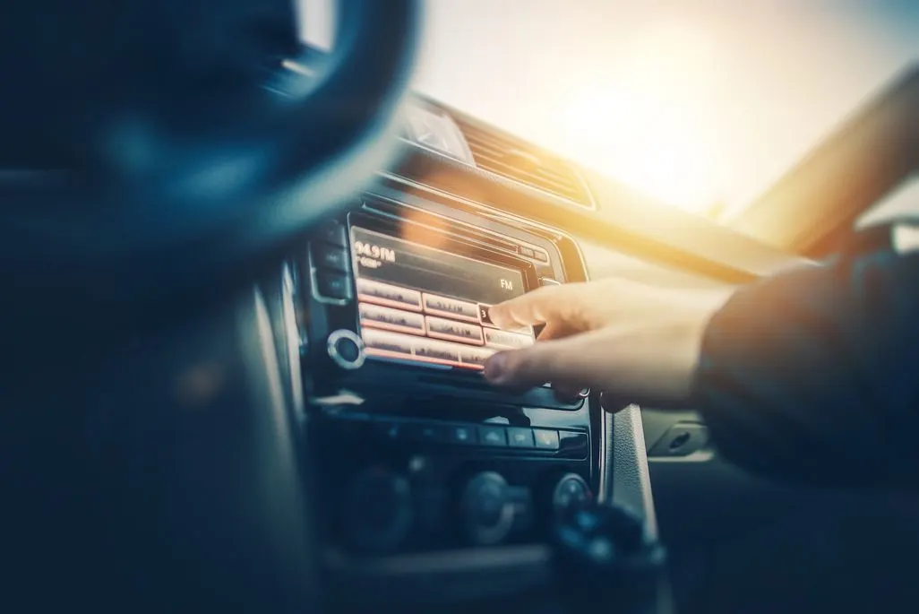 Hand bedient Autoradio mit Display in einem Auto bei Sonnenlicht