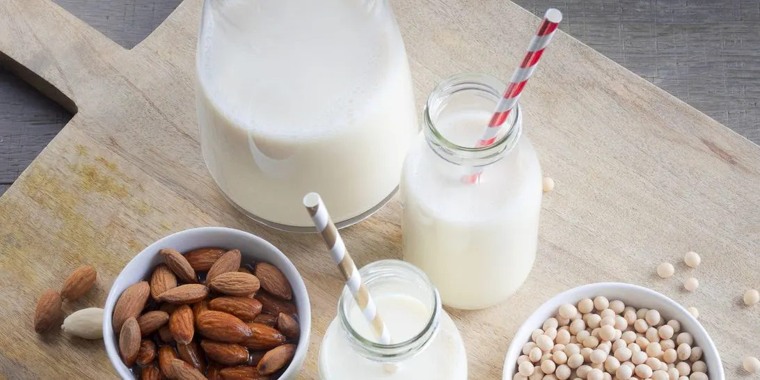 Mandeldrink und Sojadrink in Flaschen mit Strohhalmen, daneben Mandeln und Sojabohnen.