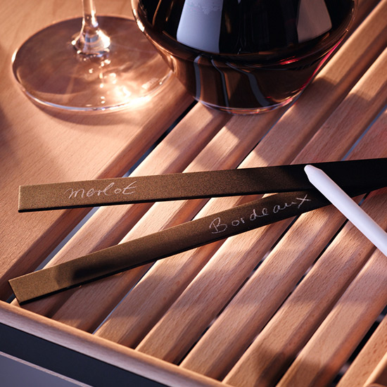 Ein Weinglas und Etiketten mit "Merlot" und "Bordeaux" liegen auf einem hölzernen Weinregal.