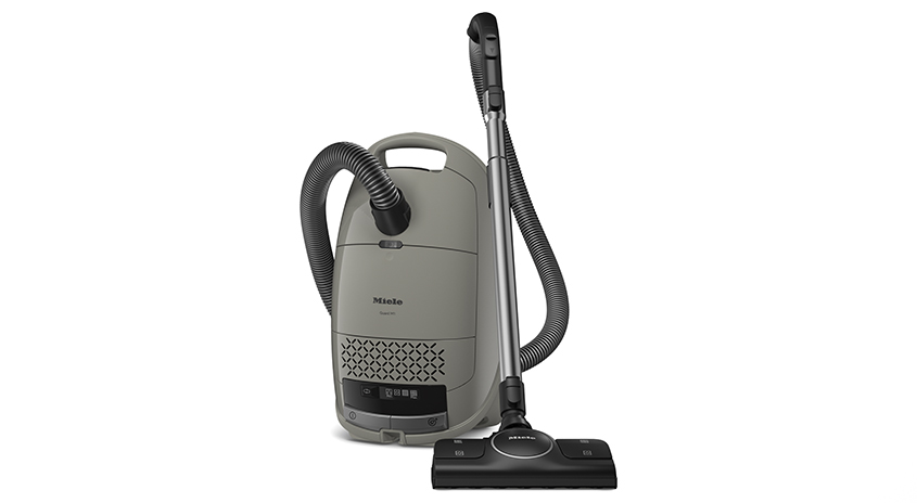 Ein grauer Miele-Staubsauger mit Schlauch und Teleskopstiel steht auf einem weißen Untergrund.