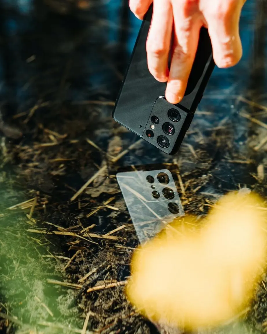 Hand hält Smartphone über eine Wasseroberfläche mit Spiegelung des Geräts.