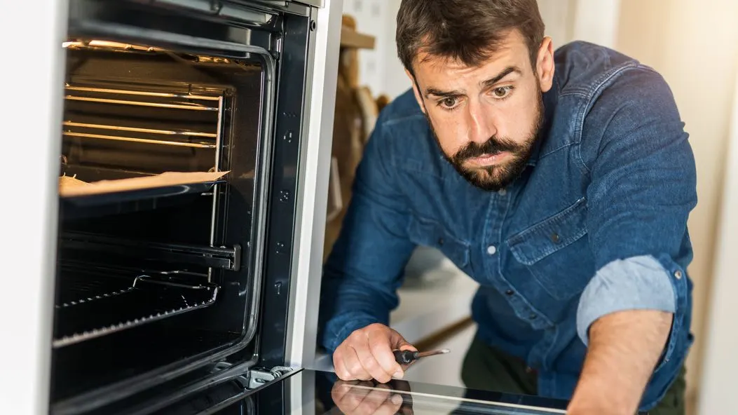 Person in Jeanshemd überprüft mit Schraubendreher einen eingebauten Backofen