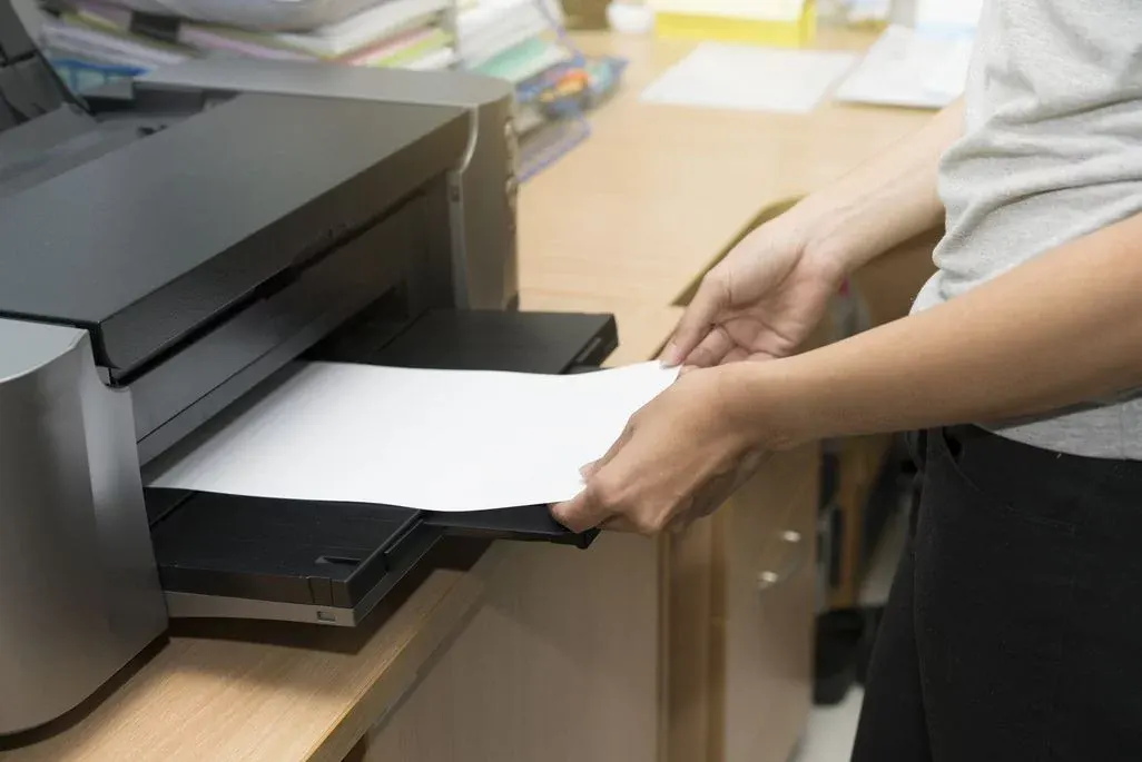 Person entnimmt bedrucktes Papier aus Drucker auf Schreibtisch.