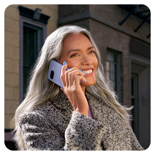 Eine Person telefoniert mit einem hellblauen Mobiltelefon vor einem Gebäude mit Fenstern und einer dunklen Fassade.