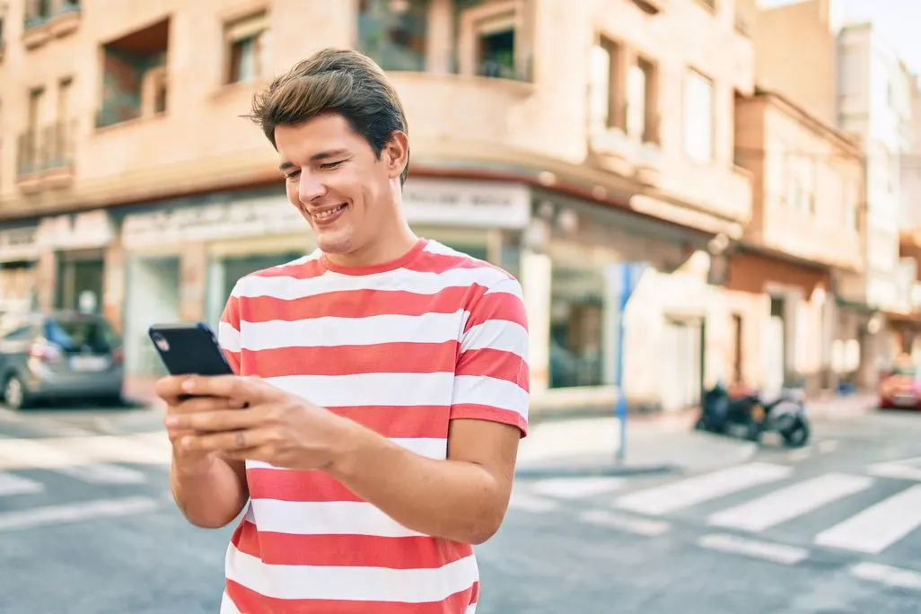 Mann im rot-weiss gestreiften T-Shirt nutzt ein Smartphone an einer Strassenecke