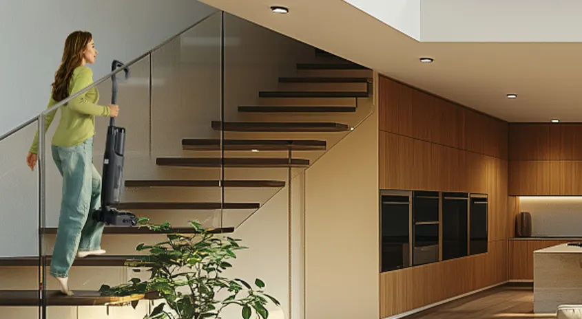 Eine Treppe mit Holzstufen und Glasgeländer führt in ein modernes Interieur mit Holzwand und Küchenbereich.