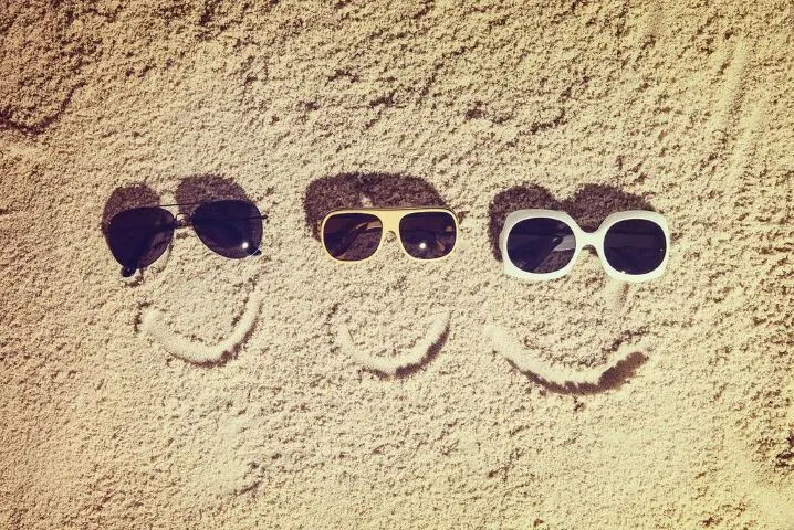 Sandstrand mit drei Sonnenbrillen und gezeichneten Mündern die 3 Smilies darstellen