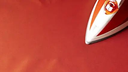 Ein rotes Bügeleisen bügelt über einen roten, glänzenden Stoff.