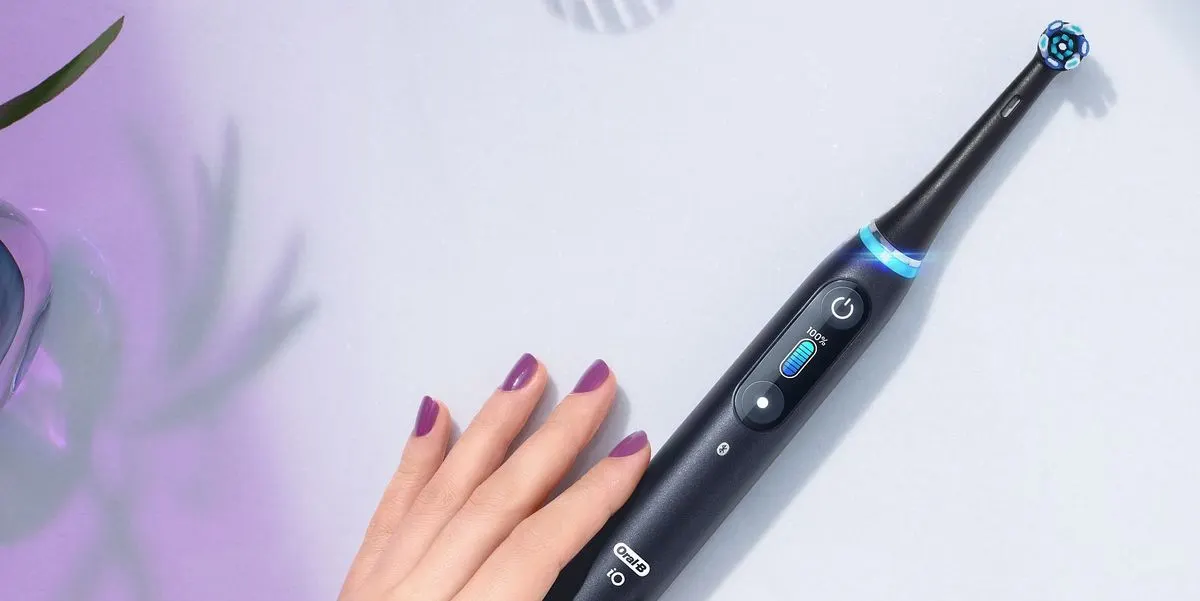 Hand mit lila lackierten Nägeln liegt neben einer schwarzen elektrischen Zahnbürste.