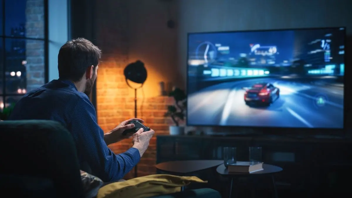 Eine Person sitzt auf dem Sofa und spielt ein Rennspiel auf einem großen Fernseher.