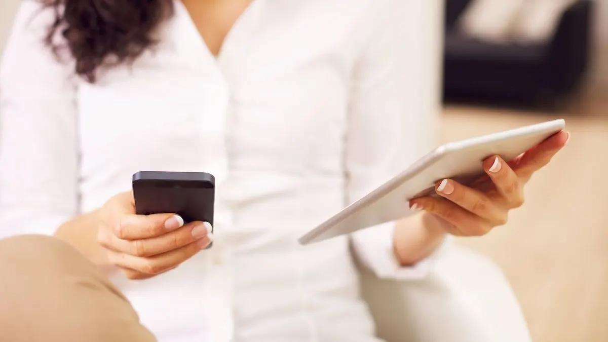 Frau hält ein Smartphone in der einen und ein Tablet in der anderen Hand.
