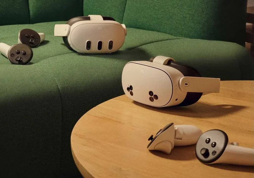 Eine Meta Quest 3 liegt auf einer Couch im Hintergrund, davor auf einem Tisch die Meta Quest 3s - alle mit ihren Joy-Cons.