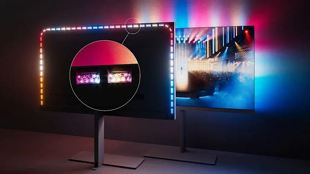 Zwei Philips OLED-Fernseher auf silbernen Standfüßen nebeneinander: Links ist die Rückseite eines Fernsehers zu sehen, dessen Ambilight-LED-Leiste entlang der gesamten Kante in Weiß, Blau, Gelb und Rot leuchtet. Ein kreisförmiger Zoom-Ausschnitt hebt zwei einzelne LED-Module in Pink und Weiß hervor. Rechts zeigt der zweite Fernseher von vorne eine Konzertbühne, während das Ambilight die Wand hinter dem Gerät in Pink, Blau und Rot anstrahlt.