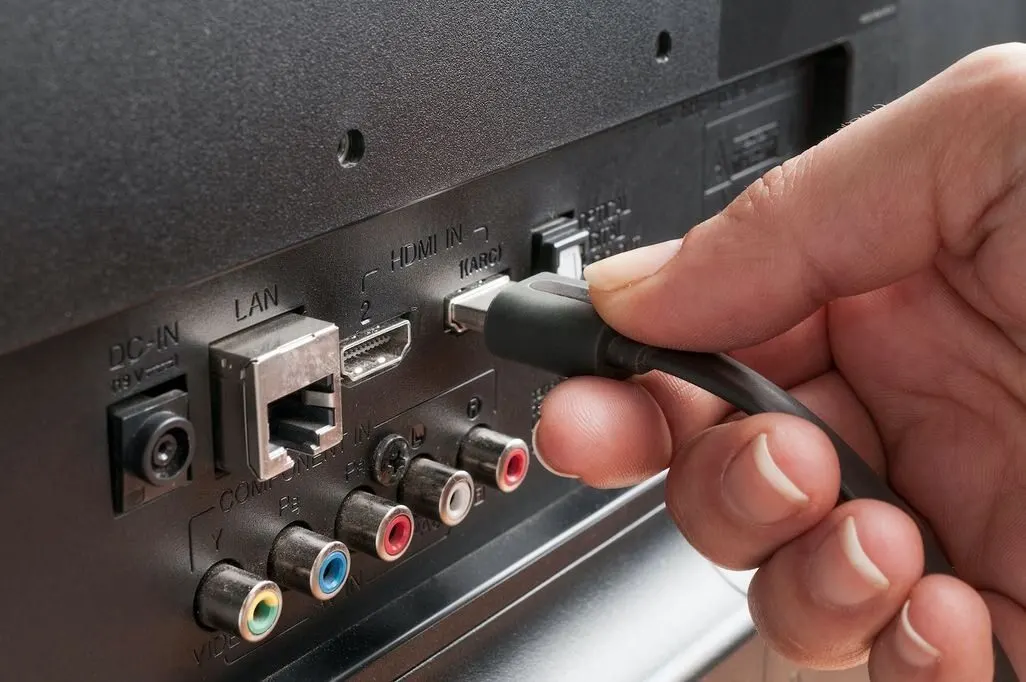 Eine Hand steckt ein HDMI-Kabel in den Anschluss eines Fernsehers