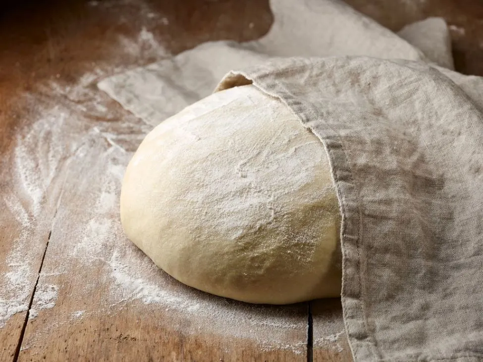 Germteig geht unter einem Tuch auf bemehlter Holzoberflaeche