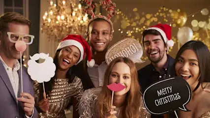 Sechs lächelnde Personen halten festliche Fotorequisiten: Weihnachtsmann-Hüte, Rentiergeweih, Bart, Brille, Lippen und Sprechblasen mit "HO HO HO!" und "Merry Christmas".