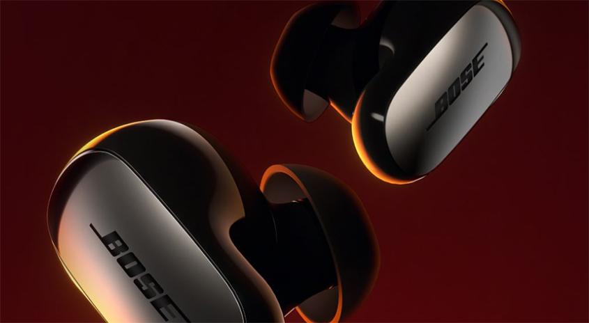Zwei schwarze Bose-Ohrhörer mit grauer Aufschrift schweben vor einem roten Hintergrund.